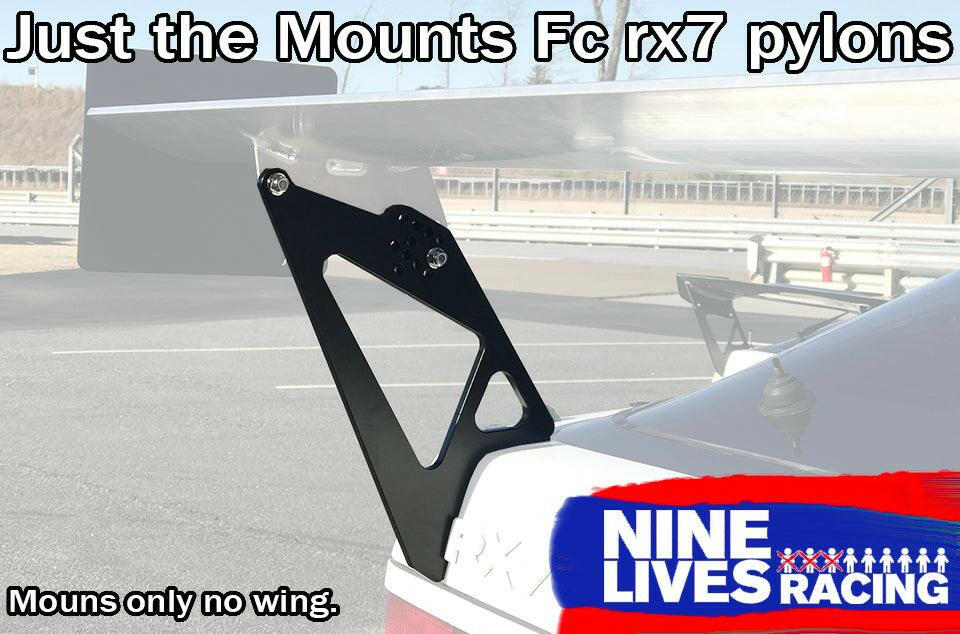 A car is equipped with an aftermarket aluminum Fc Rx7 Wing Mounts - Pylons Only kit by 9livesracing. These mounts are designed to support a spoiler, but the spoiler is not present. The background shows an empty road and a safety barrier. The text reads, "Just the Mounts FC Rx7 pylons" and "9livesracing".