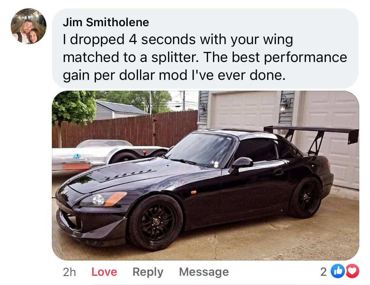 An S2000 Big Wang Trunk Mount Kit '99-09 AP1/AP2 sports car from 9livesracing, featuring a sleek black design and a large rear wing, is parked outside in front of a wooden fence. A Facebook comment above the car reads, “I dropped 4 seconds with your wing matched to a splitter. The best performance gain per dollar mod I've ever done.”
