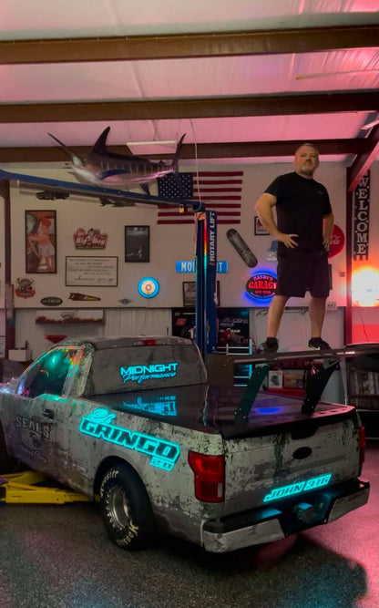 Photo of a person standing on a chassis mounted wing kit attached to there F150 race truck in a shop