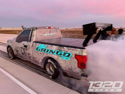 The image shows a pickup truck with a large rear wing attached to the chassis, marketed as the 'F150 Big Wáng Chassis mount kit'. The truck is participating some sort of racing event, indicated by the 'GRINGO' livery and racing decals.