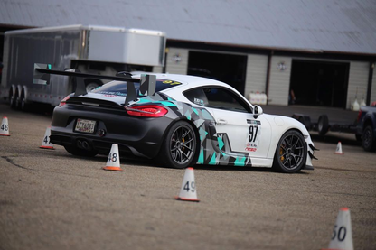 A Porsche Cayman with a rear wing spoiler, displayed on a track.