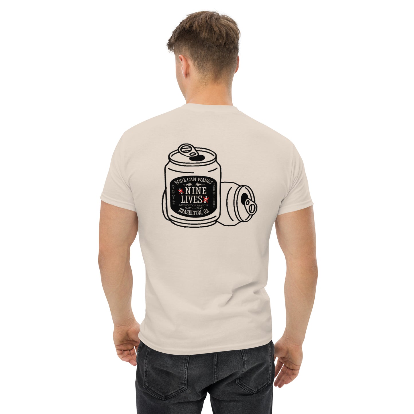 A man stands facing away, wearing a beige Men's Soda Can Wang t-shirt by Nine Lives Racing. The 100% cotton classic tee showcases an illustration of crumpled soda cans and a bold black and red label reading "Soda Can Hardly, Nine Lives, Houston, CA" on the back—ideal for layered streetwear outfits.