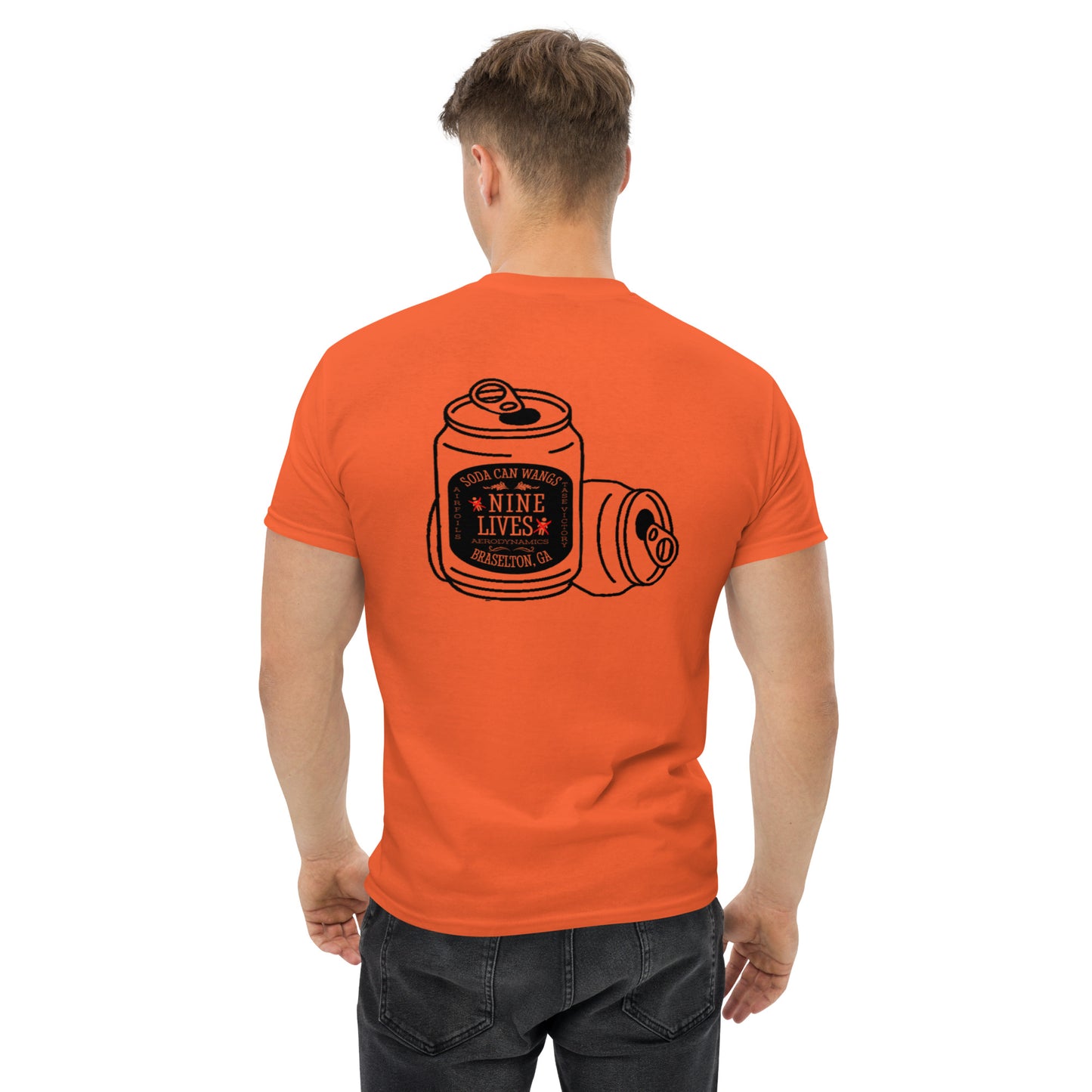 A man with short hair, seen from behind, is wearing an orange Men's Soda Can Wang t-shirt by Nine Lives Racing. The back of the 100% cotton tee features an illustration of soda cans with the text "Soda Can Mafia Nine Lives" and "Beloit, WI" written on one of the cans. He is also wearing dark jeans, perfect for layered streetwear outfits.