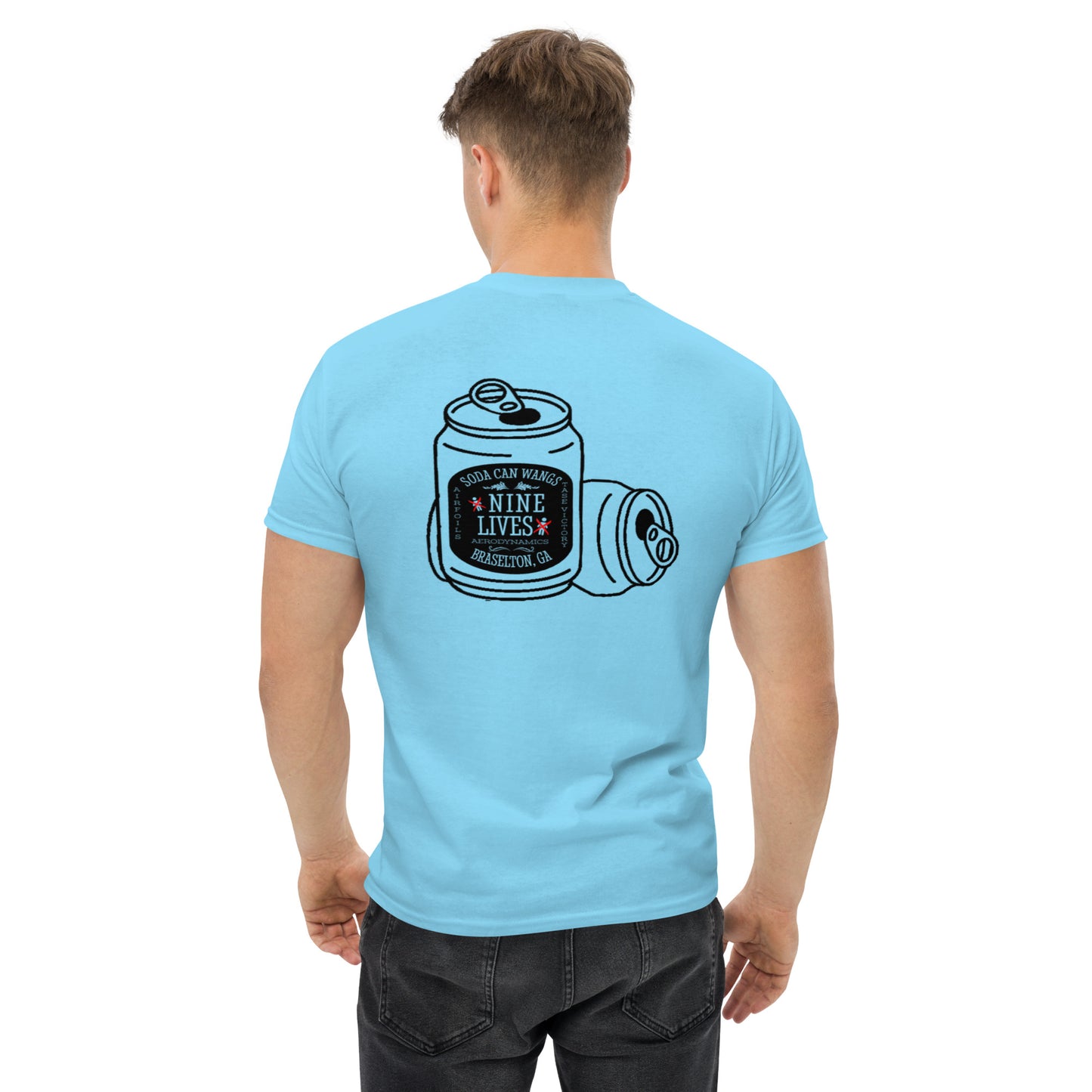 A person with short hair, wearing a light blue Men's Soda Can Wang t-shirt by Nine Lives Racing made of 100% cotton, is facing away. The back of the shirt features a graphic of two soda cans with the text "NINE LIVES" in a small central label. The background is plain white.