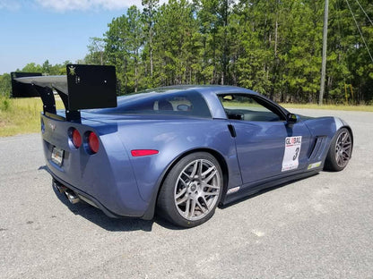 A blue sports car equipped with a 9livesracing Corvette Medium Downforce Kit ‘97-04 C5 is parked on an asphalt surface, with trees in the background. The car features sleek design lines, silver alloy wheels, and a racing sticker on the side displaying the number 3.