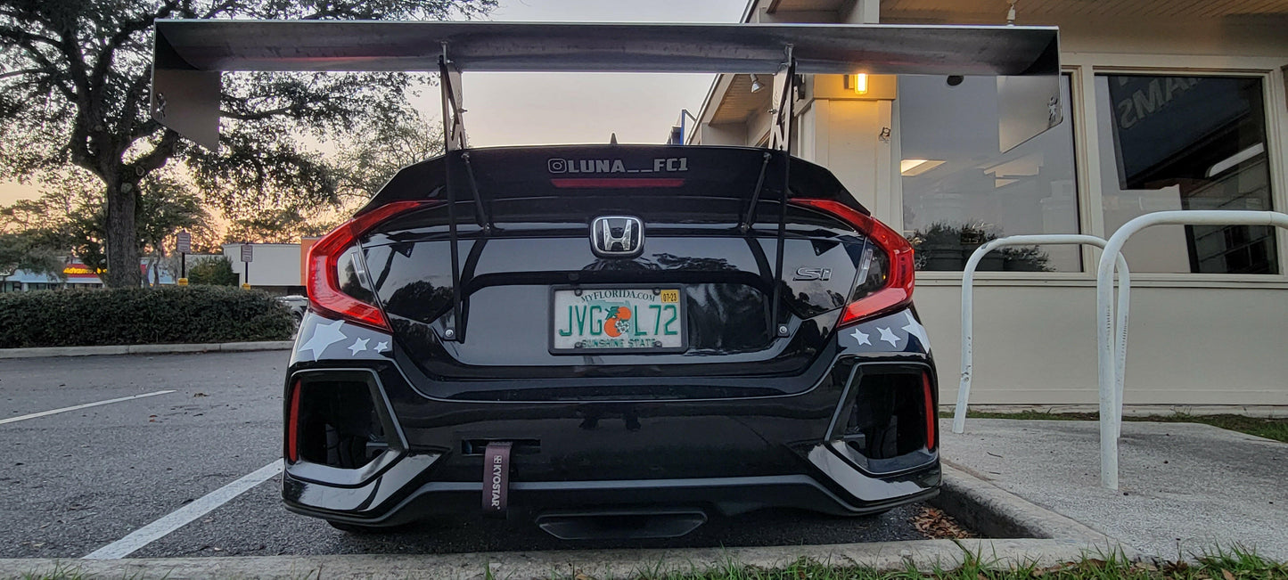 A modified black Honda Civic Si, enhanced with the Civic Wang kit 2017+ FC1 from 9livesracing and sporting a large rear spoiler, is parked outside a building. The vehicle has a Florida license plate reading "JWC L72" and features a custom decal on the rear window reading "@LUNA_FCI." The car, equipped with aluminum wings from the kit for added downforce, is decorated with white star patterns.