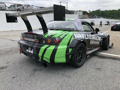 A race car showcasing a black and green striped design with branding for 9livesracing and Speed Freaks USA is parked in a lot. Equipped with The Deuce! Double Element Kit, the American-made car proudly displays the number 771 on its side window. Other vehicles and a white wall can be seen in the background.