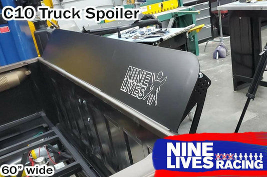 Image of a 60-inch wide C10 1967-72 truck spoiler kit made from sturdy 6061 aluminum installed on a vehicle. The spoiler features "9livesracing" and a logo on it. The text "C10 Truck Spoiler Kit" is at the top left, and "60'' wide" is at the bottom left. The workshop setting has various tools and equipment in the background.