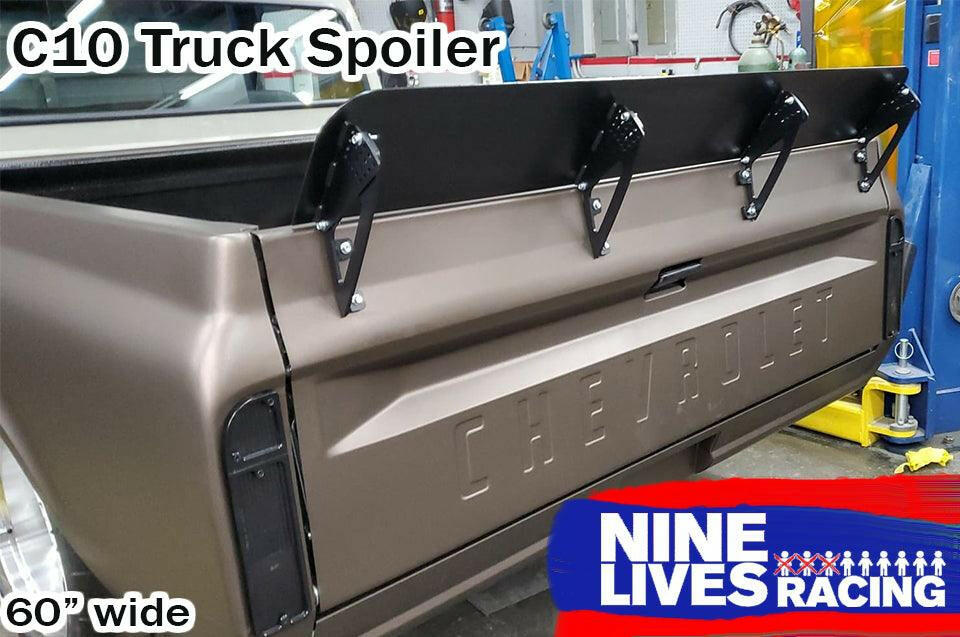 Image of a Chevrolet truck's rear view featuring a black spoiler attached to the tailgate. Text on image: "C10 1967-72 Truck Spoiler Kit", "9livesracing", and "60” wide". The 6061 aluminum spoiler is designed to boost downforce. The truck is parked in a workshop with various tools and equipment visible.