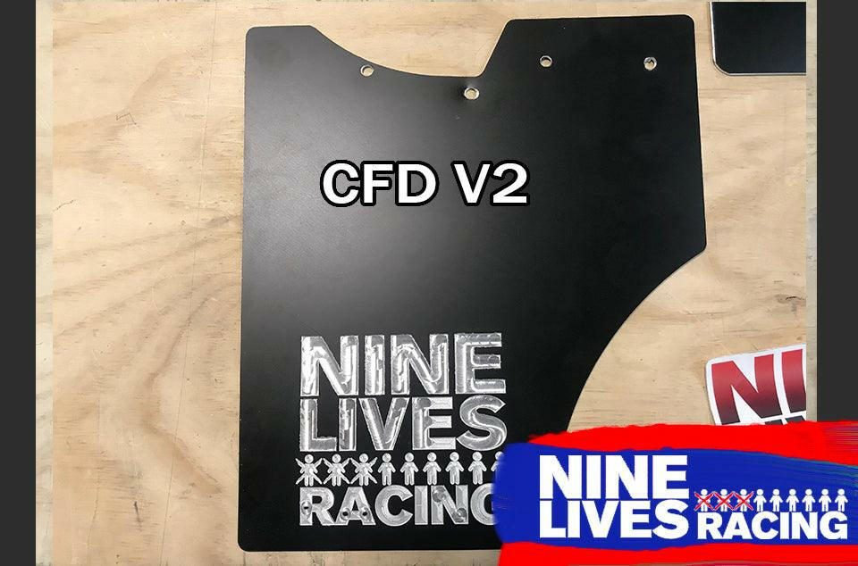 A black aluminum car part with the text "CFD V2" engraved on it is positioned on a wooden surface. Below the text, there is a logo with the words "NINE LIVES RACING" and small icons of people. End Plates for The Big Wáng! are visible near the corner, along with another 9livesracing logo in blue, white, and red.