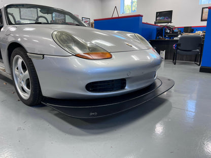 Front-end of a Porsche Boxster 986 featuring a black splitter attached to the bumper,.