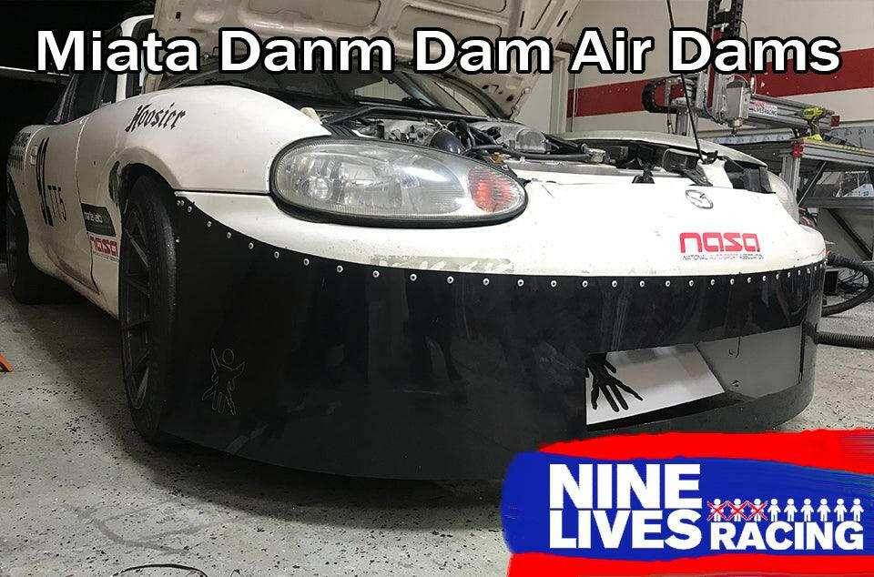A white Mazda Miata race car with a black front air dam is in a garage with its hood open. The text "Miata Damn Dam '90-05 NA/NB" is at the top of the image, while the "9livesracing" logo sits at the bottom right corner, emphasizing their commitment to downforce.