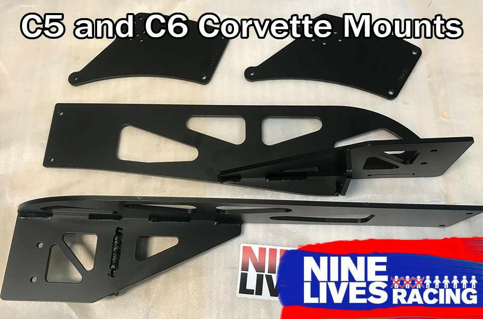 Black metal automotive mounting brackets are laid out on a flat surface. The text "Corvette C5/C6 Mounts - Pylons Only" is at the top of the image. At the bottom is a red and blue logo with the words "9livesracing." These aluminum mounts exemplify durability for C5/C6 Corvette enthusiasts.
