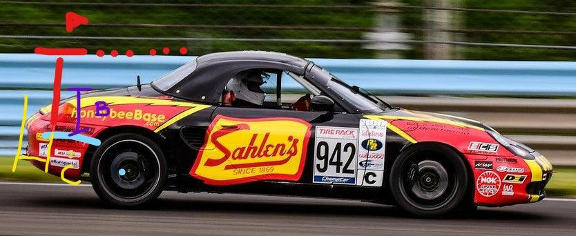 A red and black race car with the number 942 is speeding on a track, its 9livesracing Custom Chassis Mount kits ensuring a consistent drive. The car features various sponsor logos, including a prominent "Sahlen's" logo on the door. The background is blurred, indicating motion. Red, blue, and yellow markings are edited on the image.