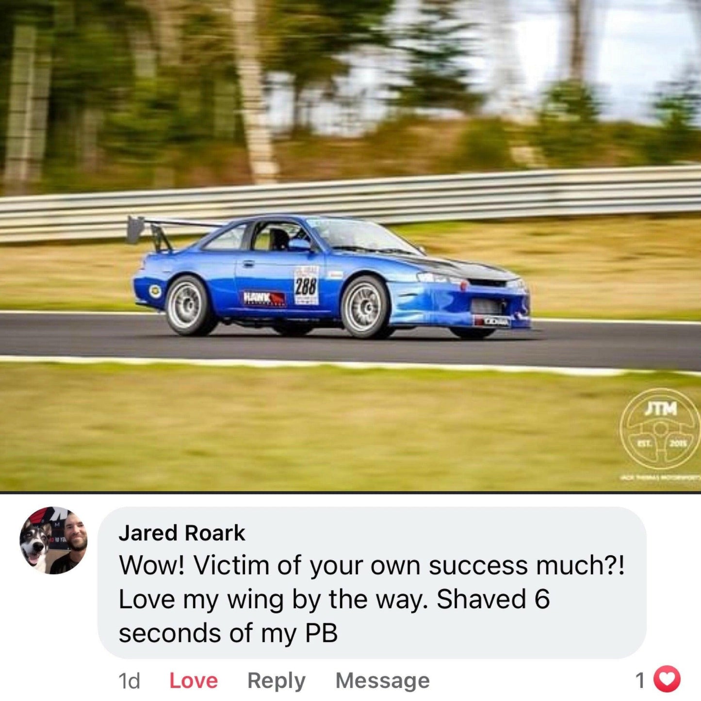 A blue race car with the number 288 on its side speeds around a track under The Builder's Big Wáng - Spec Your Own Size by 9livesracing. The background shows blurred trees, indicating motion. Below the image, a social media comment says, "Wow! Victim of your own success much?! Love my wing by the way. Shaved 6 seconds off my PB.