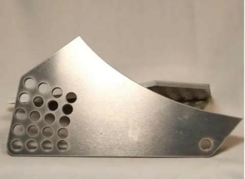 A close-up image of the 9livesracing Just the Wáng Mounts, crafted from shiny 6061 aluminum. The mount features a series of circular holes on the left side, a smooth curved top edge resembling a wing, and a small circular hole on the bottom right. The background is a plain, light-colored surface.