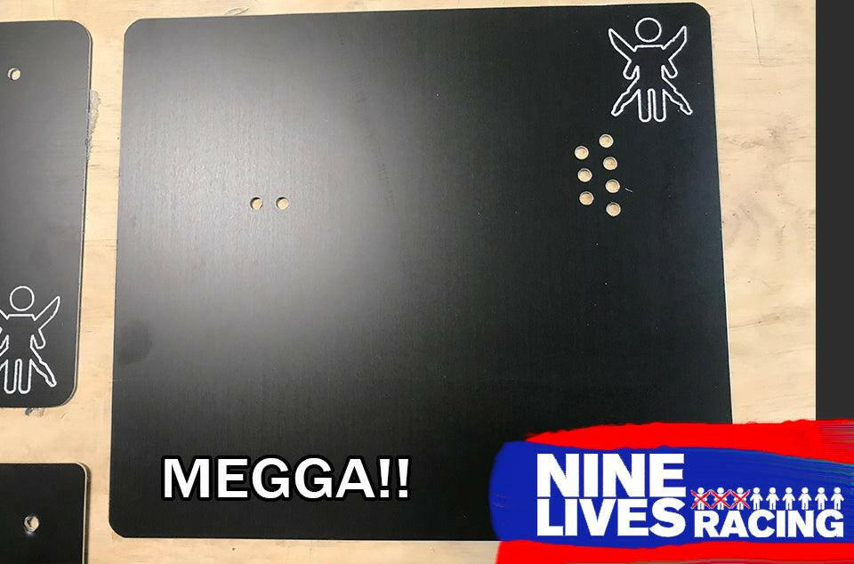 An End Plate for The Big Wáng! by 9livesracing is a rectangular black aluminum plate with holes arranged in a circular pattern on the right side. A small, white line drawing of a person is situated in the top right corner, while the bottom right features a red and blue graphic bearing the text "NINE LIVES RACING." The word "MEGGA!!" overlays on the left.