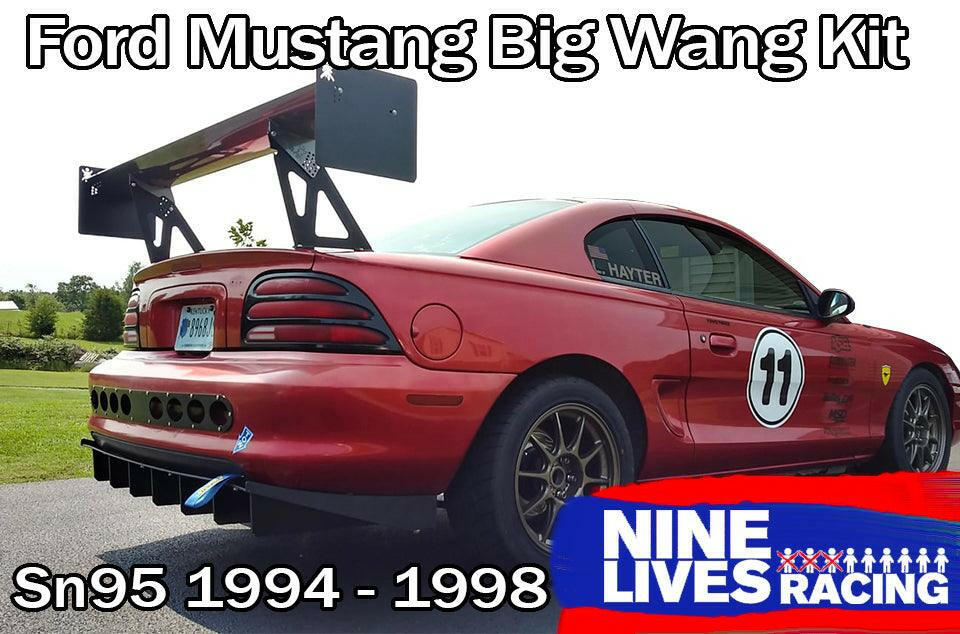 A red Ford Mustang from the 1994-1998 SN95 series is parked on asphalt, featuring a large extruded aluminum wing from the 9livesracing Mustang Big Wang Kit '94-'98 SN95. The car sports race decals including the number 11 and aftermarket wheels. Text reads "Mustang Big Wang GT3" and "9livesracing," highlighting its impressive lift to drag ratio.