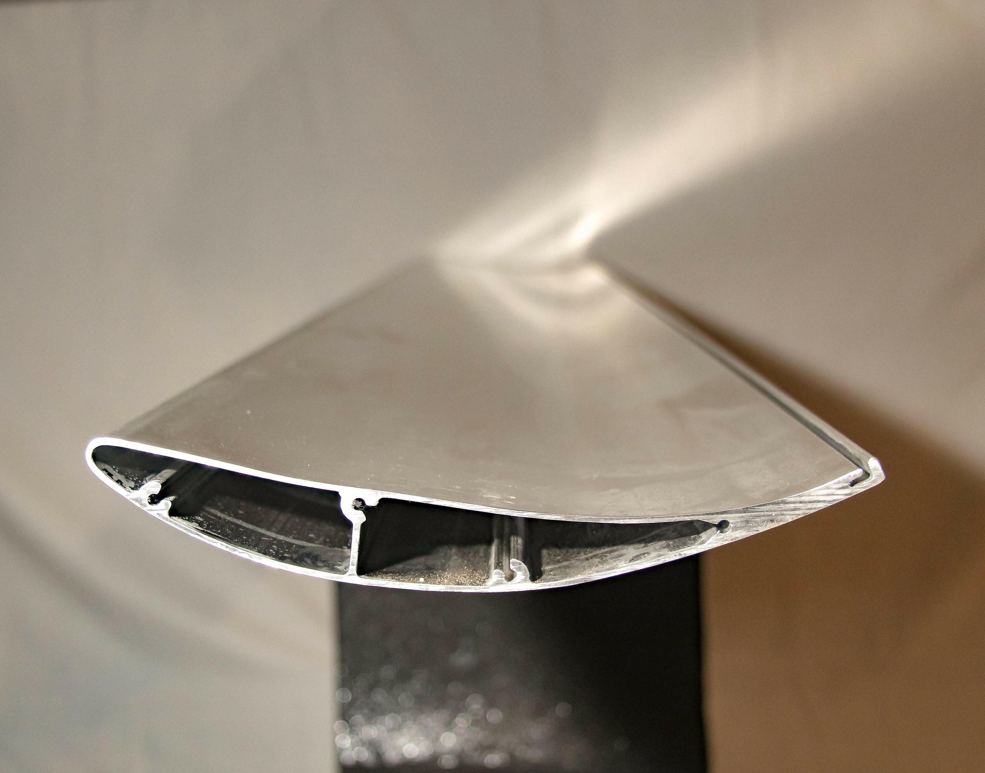 Close-up of the cross section of an Integra V2 Big Wang Kit '94-01 DC2 by 9livesracing. The image captures the detailed internal structure and aerodynamic design, emphasizing low drag with the leading edge positioned at the top and the aerodynamic surface clearly visible. Supported by endplate mounts, the wing is displayed on a black stand.