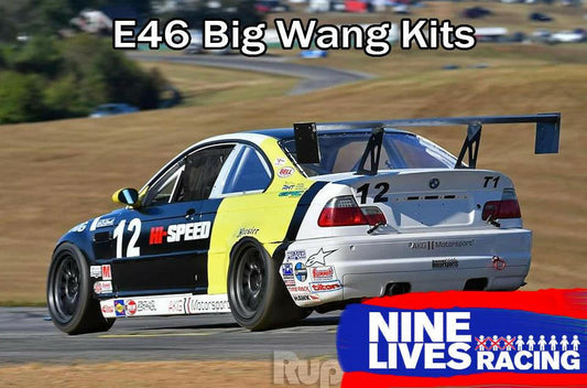 A race car with number 12 and various sponsor decals speeds on a track. The car features a large extruded aluminum rear wing with "3-Series Big Wang Kit '97-06 E46" displayed at the top. In the lower right corner, the 9livesracing logo is prominently featured. The background shows grassy hills, enhancing its lift-to-drag ratio.
