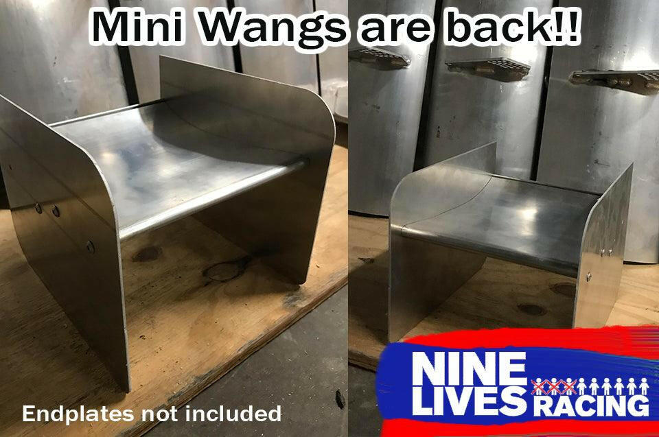 Two metal mini wing structures are displayed in a workshop setting. Text at the top reads "Mini Wangs are back!!" The bottom left states, "Endplates not included," and the bottom right showcases the 9livesracing logo in red, white, and blue colors. Ideal for enthusiasts seeking a 15:1 lift to drag ratio!