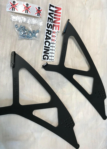 An image features two black metal brackets with multiple cutouts, a bag of screws, a Nine Lives Racing (9livesracing) sticker, and a pack of six small "Do Not Touch" stickers. The items are displayed on a light grey surface next to an extruded aluminum wing, highlighting the 350z Big Wang Kit '02-08 Z33 for superior GT3 performance.